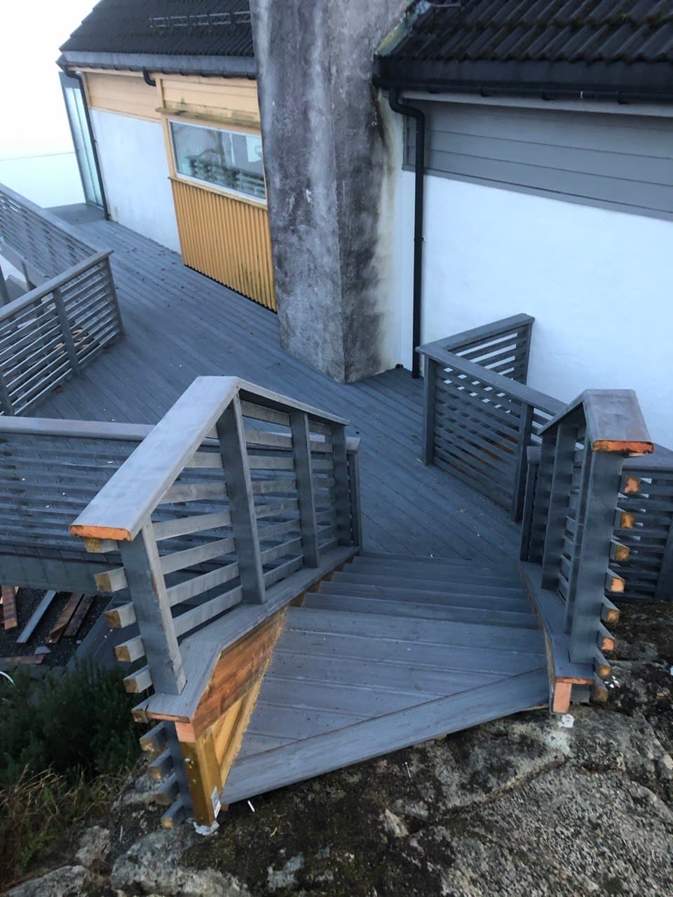 Terrasse og trapp med grått rekkverk i skrånende terreng
