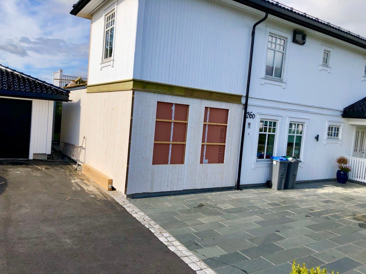 Tilbygget kledd i hvitt, med steinbelegg foran